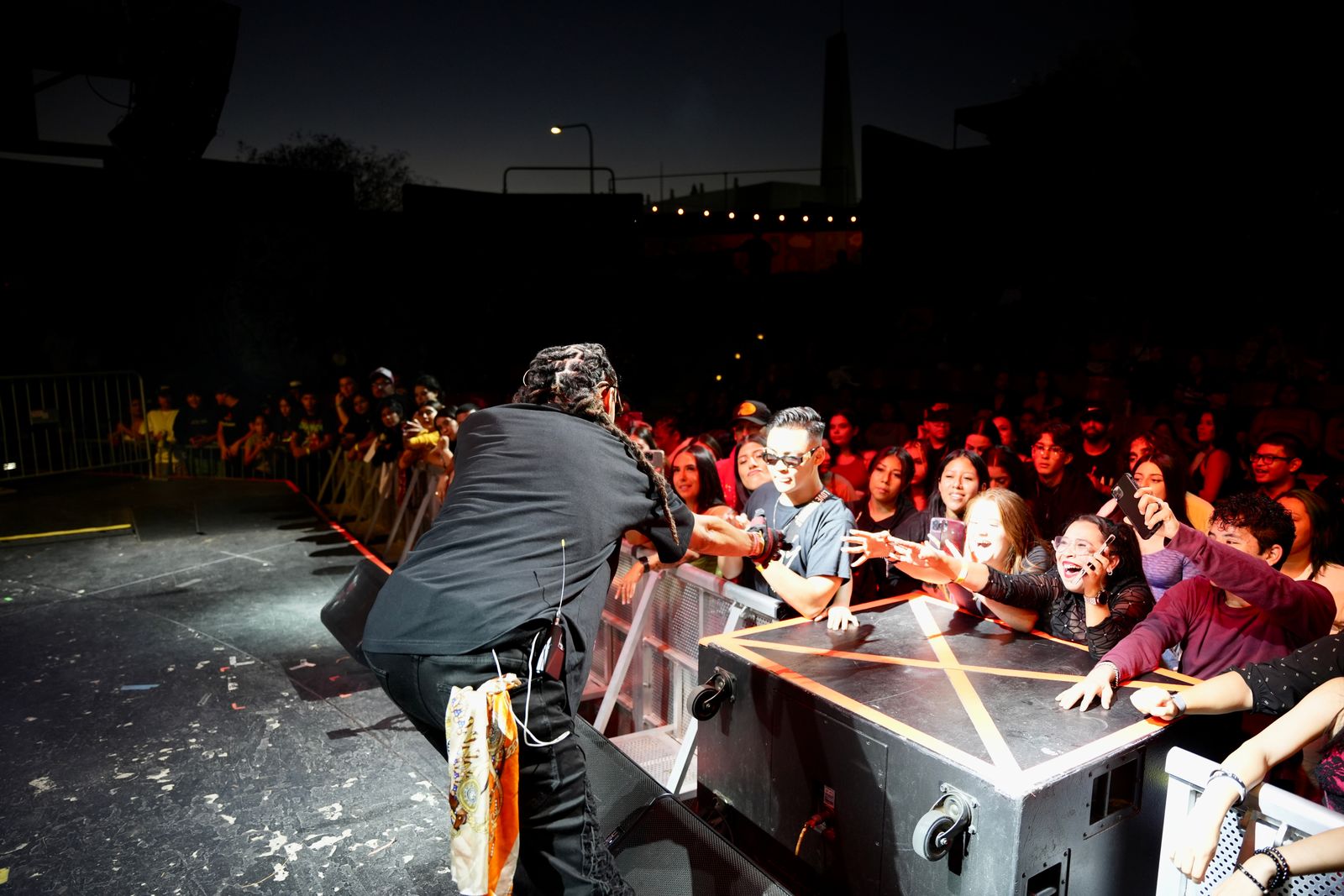 Kilohana slapping hands with fans at the barricade during an outdoor night show
