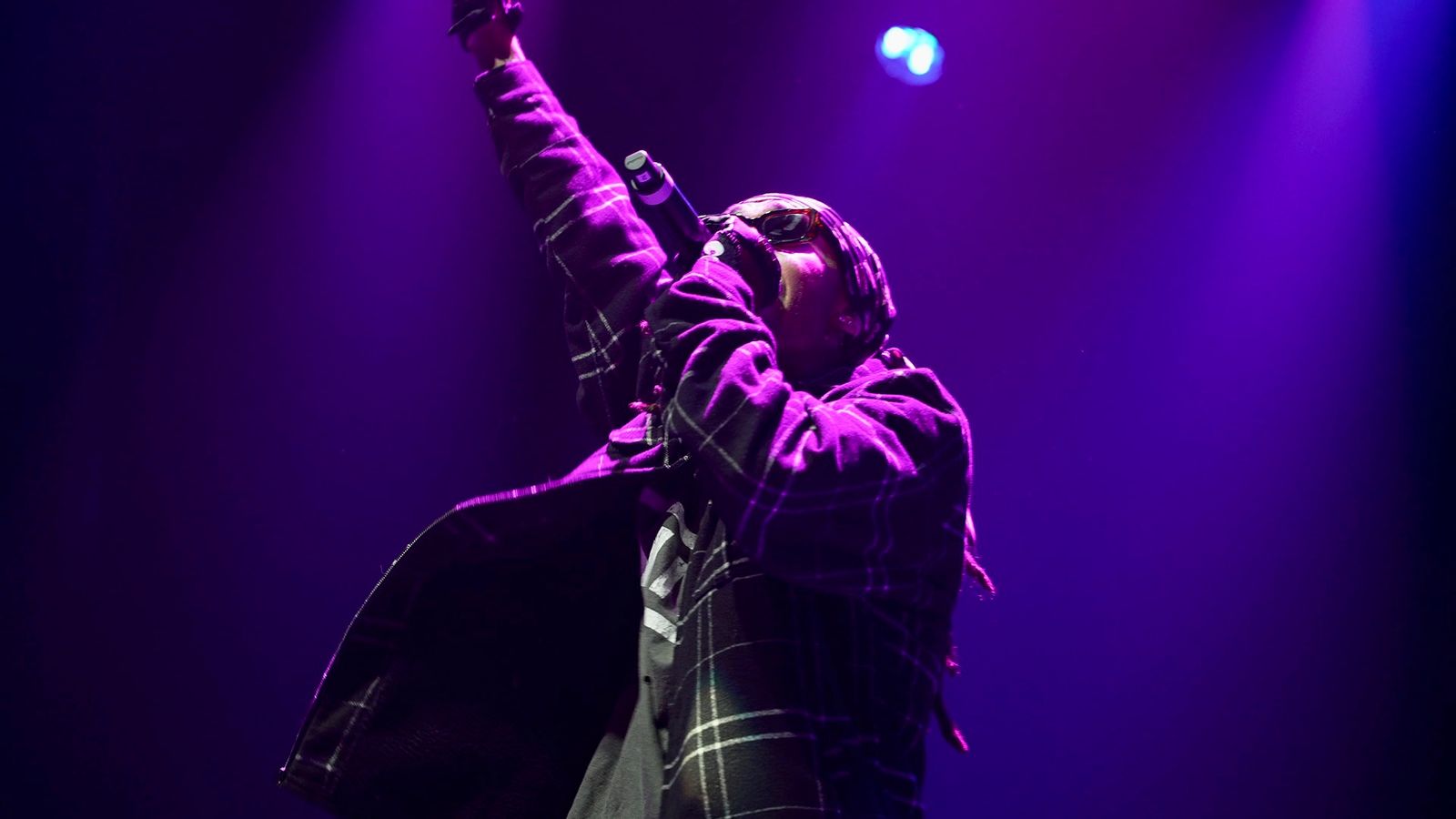 Kilohana raising one arm on stage under a purple spotlight